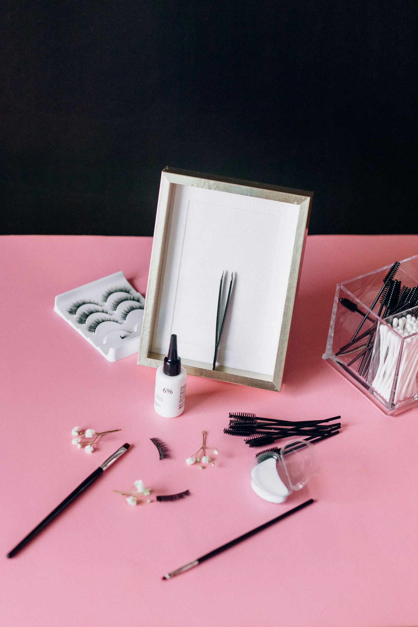 False lashes, tweezers and a small mirror on a pink tabletop