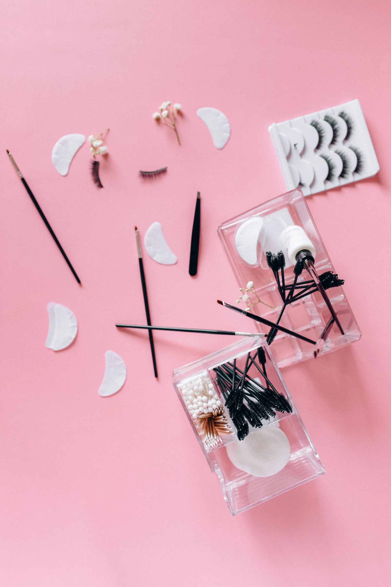Lash tweezers, under-eye pads and lash brushes on a pink background
