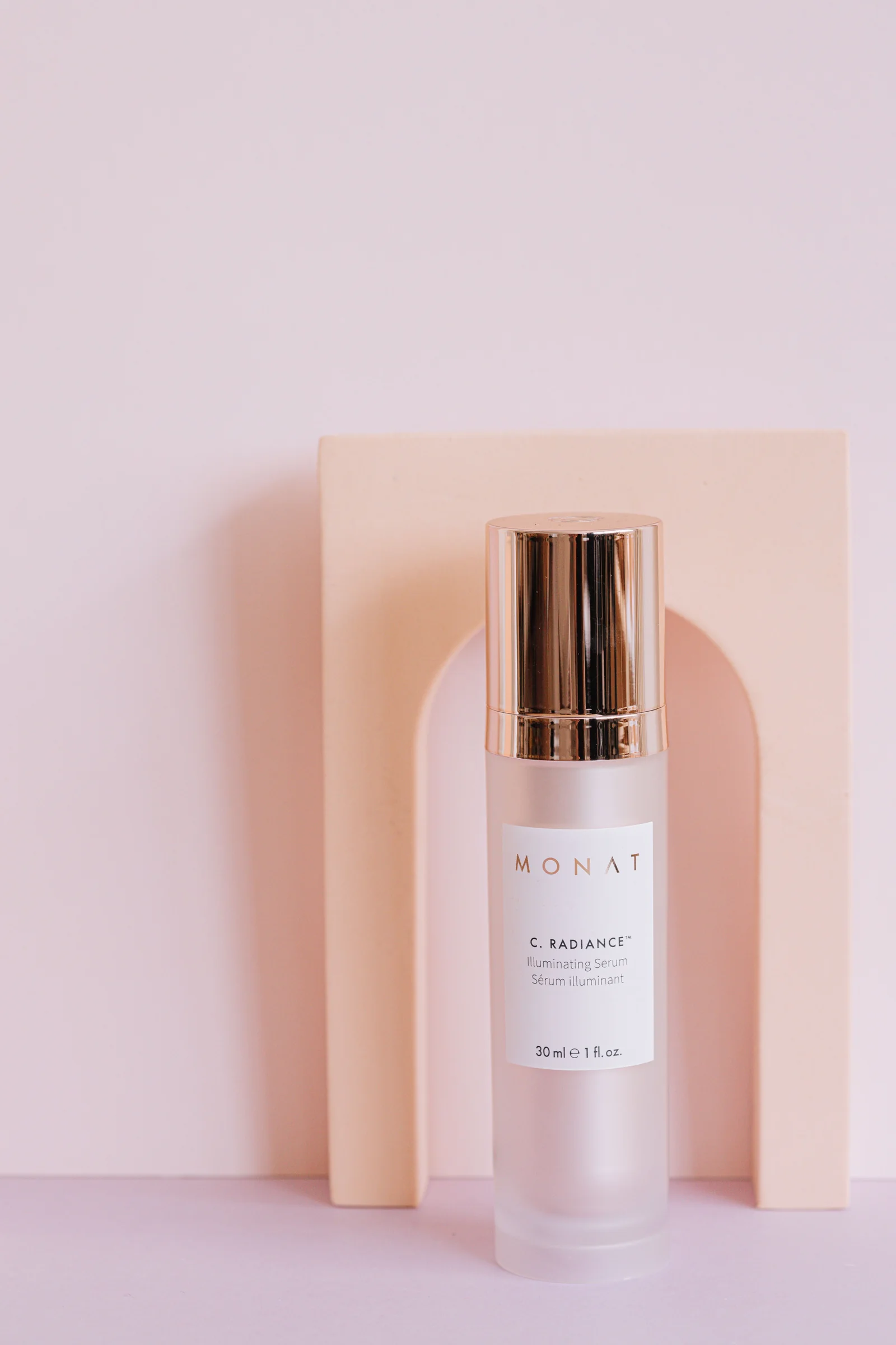 A glass serum bottle on a soft pink pedestal