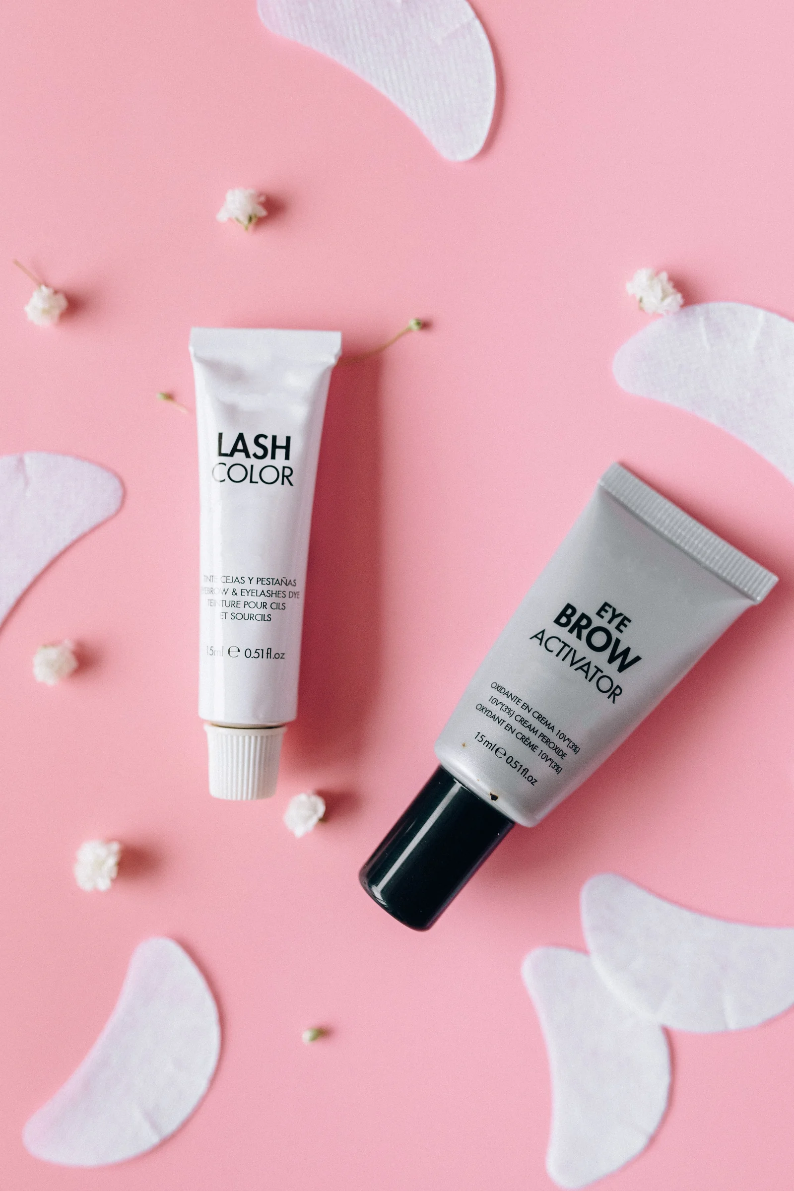 Lash and brow tint tubes and under-eye pads on a pink background